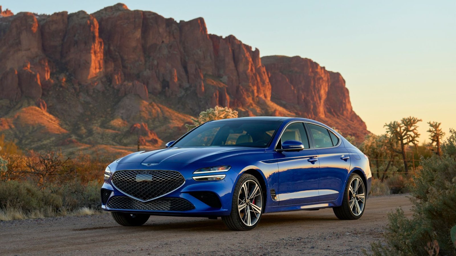 Front 3/4 shot of a blue 2025 Genesis G70 parked on gravel with a mountain in the background.