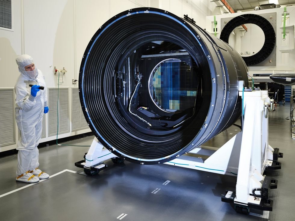 Technician examines a large telescope camera in a clean room environment.