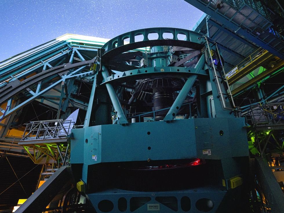 Large telescope inside observatory dome against a bright starry night sky.