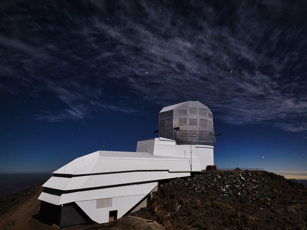 Modern observatory under a starry night sky on a rocky hilltop.