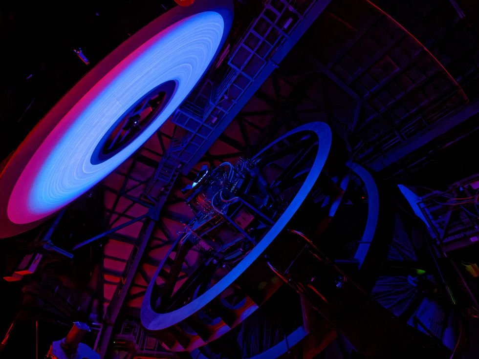 Illuminated telescope interior with vibrant blue and red hues, showcasing intricate machinery.
