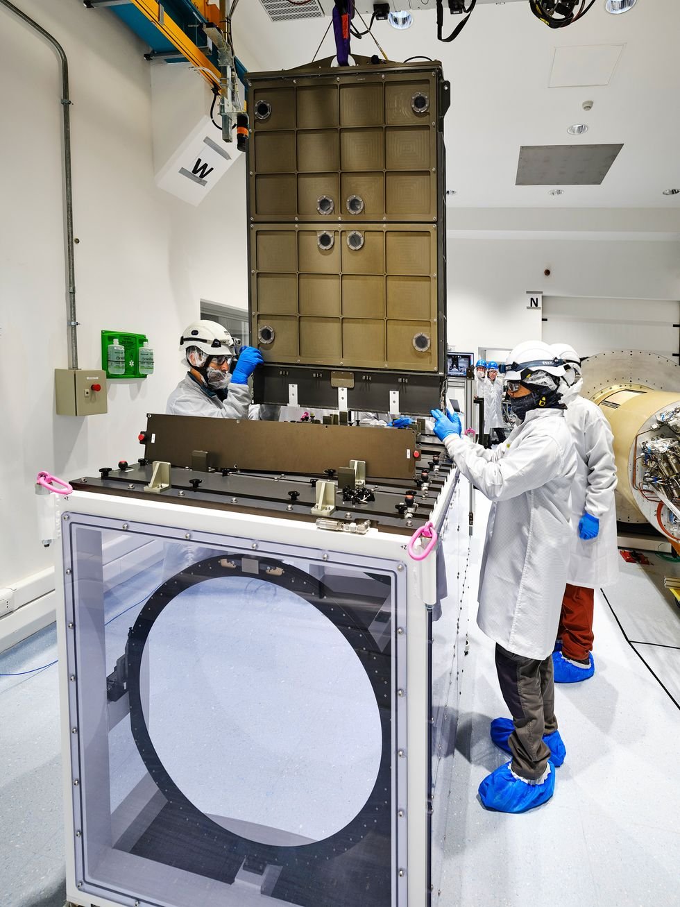 Technicians in clean suits handling a large metallic component in a laboratory.
