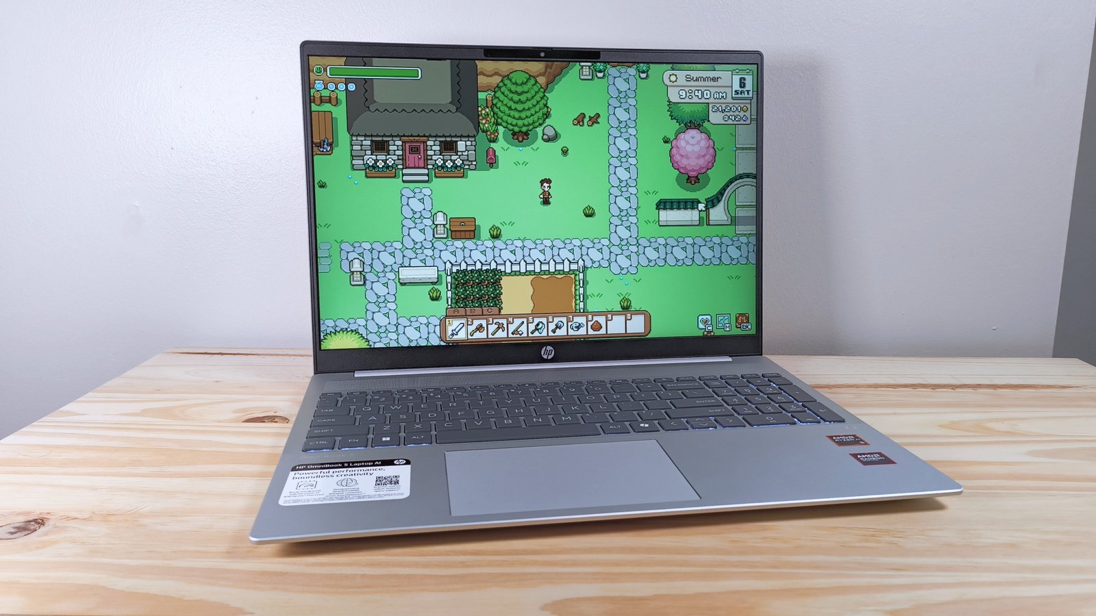 The HP Omnibook 5 Laptop AI on a wood table running Fields of Mistria