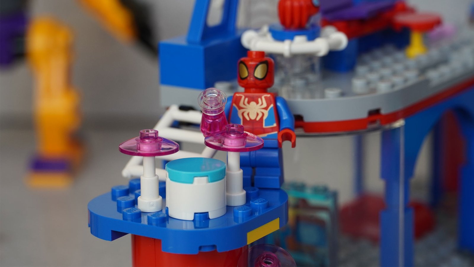 A minifigure of Spider-Man is among some colorful bricks, shaped to be a headquarters on a grey background.