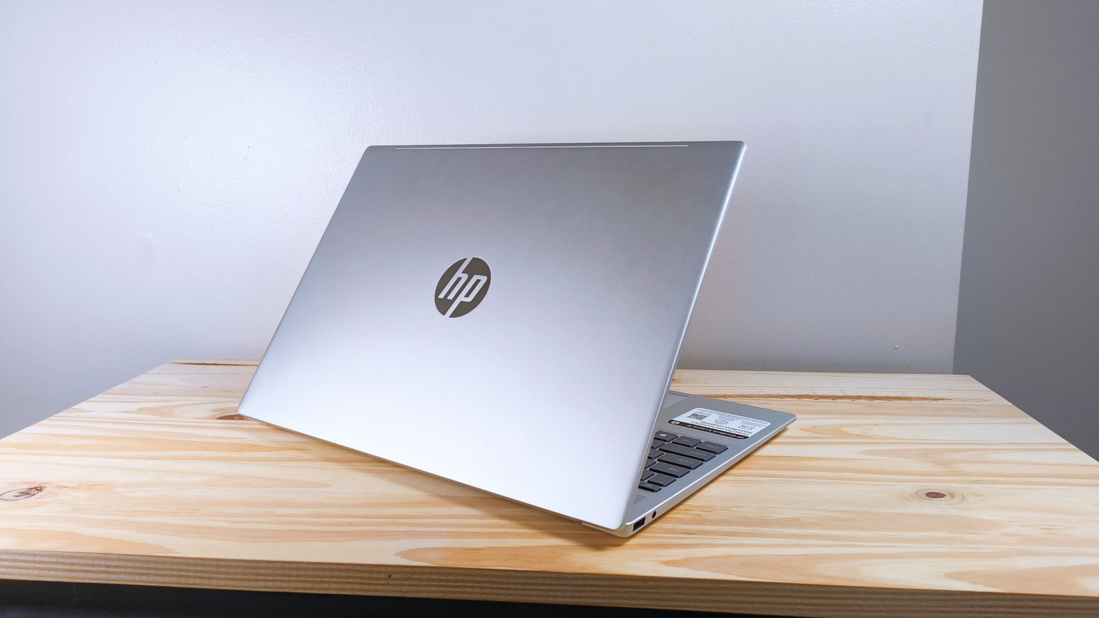 The HP Omnibook 5 Laptop AI with lid open seen from behind on a wood table