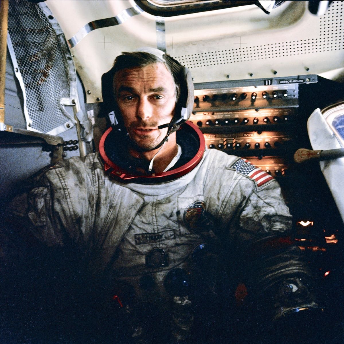 A man wearing a white space suit and helmet looks at the camera